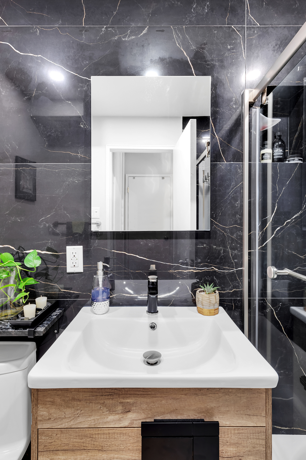 Luxury modern bathroom with dramatic black porcelain slabs featuring gold veining, custom walnut vanity, matte black fixtures, and frameless glass shower – Murray Hill Manhattan by SABI Construction