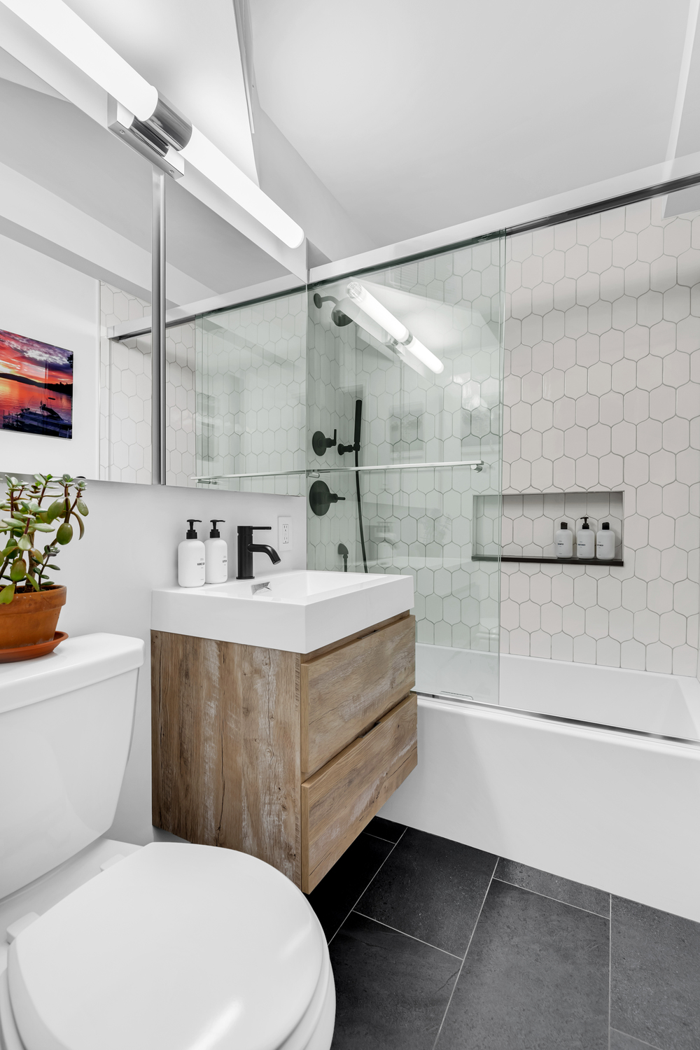 Luxury modern bathroom renovation Upper East Side Manhattan with wall-mounted walnut vanity, charcoal large-format floor tile, white subway wall tile, and alcove bathtub