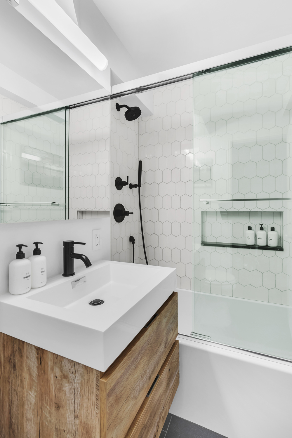 Luxury modern bathroom renovation Upper East Side Manhattan with wall-mounted walnut vanity, charcoal large-format floor tile, white subway wall tile, and alcove bathtub