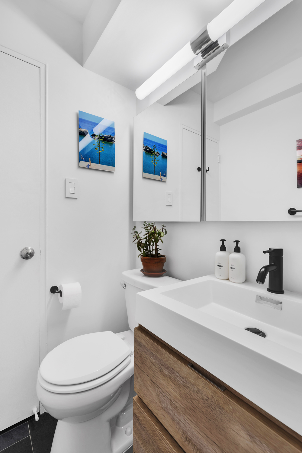 Luxury modern bathroom renovation Upper East Side Manhattan with wall-mounted walnut vanity, charcoal large-format floor tile, white subway wall tile, and alcove bathtub
