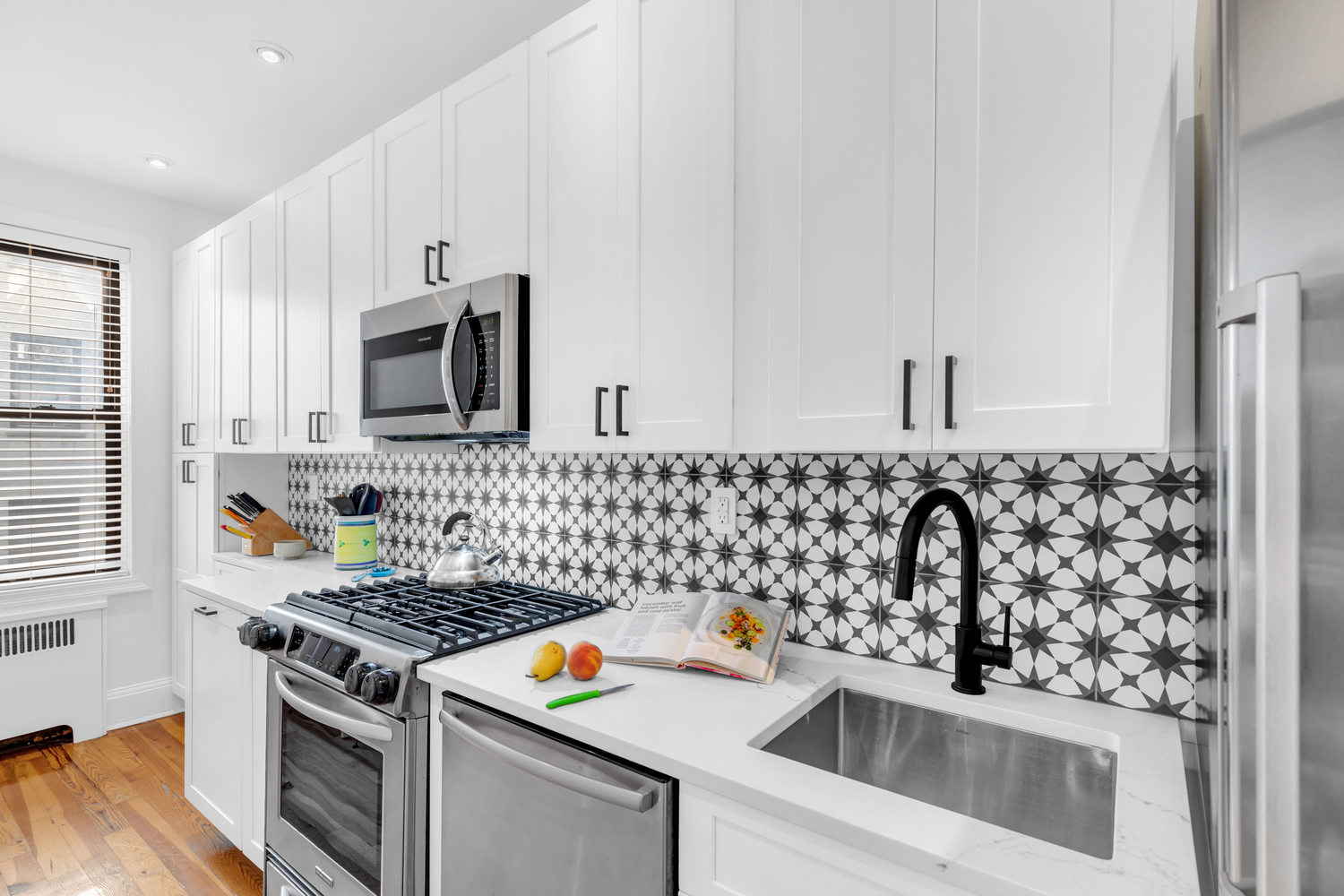 Luxury white shaker kitchen with matte black hardware, black-and-white star tile backsplash, quartz countertops, and hardwood floors – full renovation in Prospect Park Southwest, Brooklyn by SABI Construction